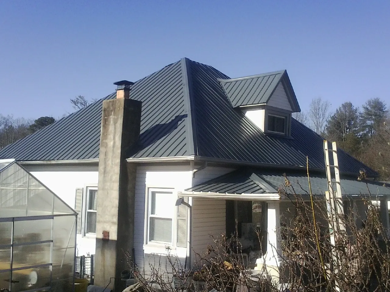 Dark blue standing seam metal roof on a white farmhouse with dormer — Slate & Tile Roof Repair by Roofing Brothers in Beech Bluff