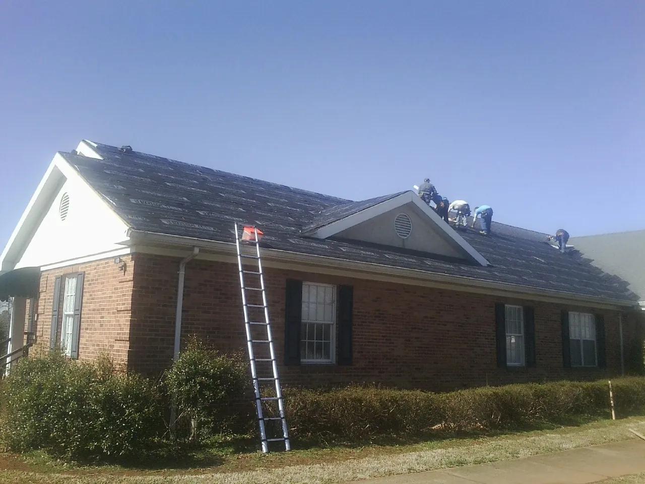 Crew tearing shingles off a brick ranch roof with a ladder set — Metal Roof Repair work by our crew in Beech Bluff