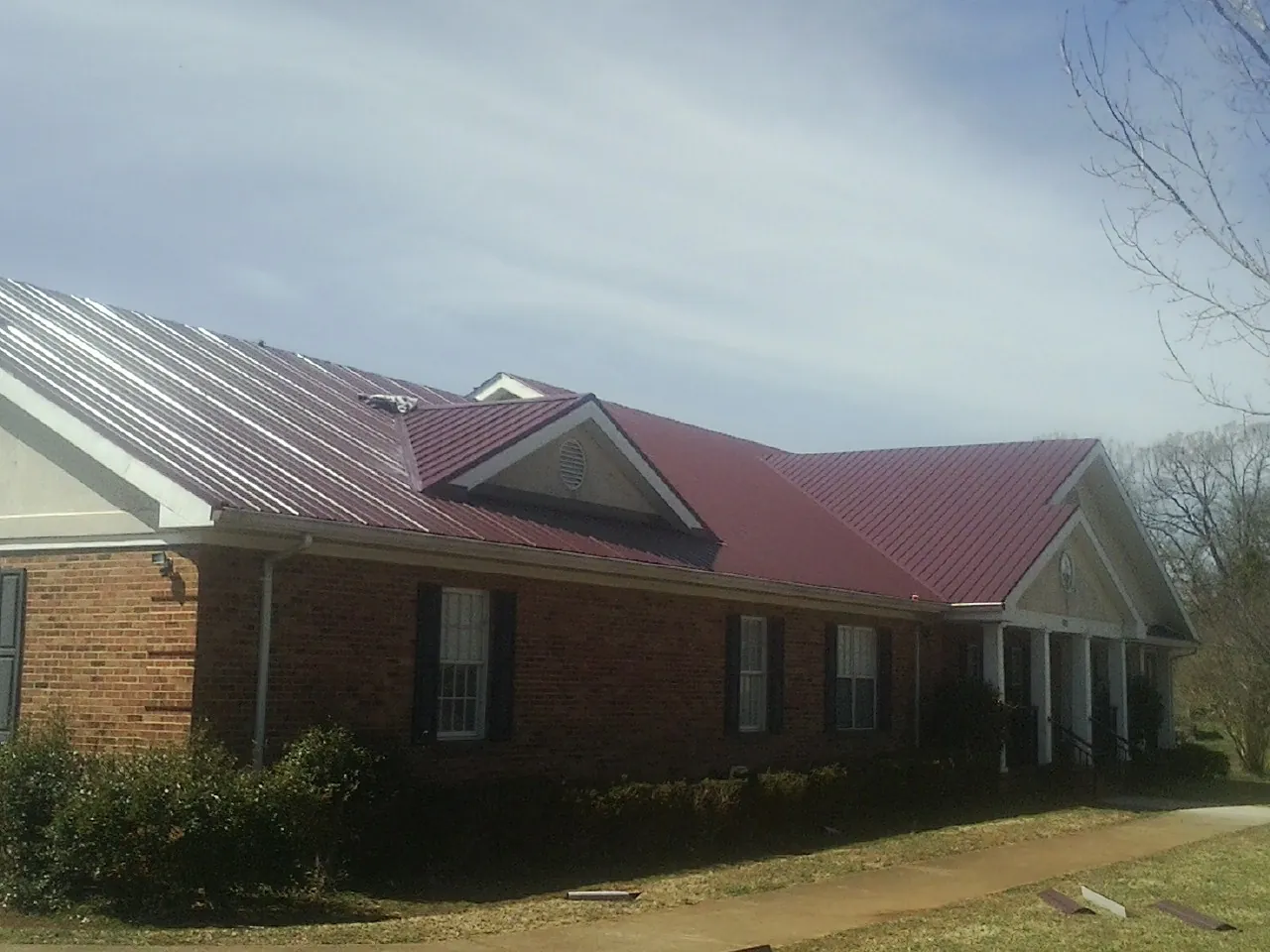 Red metal roof with gabled entries on a long brick building, from a Hail Damage Roof Repair job in Beech Bluff