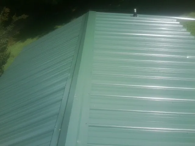 New green metal panels meeting at the ridge of a roof — Flat Roof Repair work by our crew in Beech Bluff