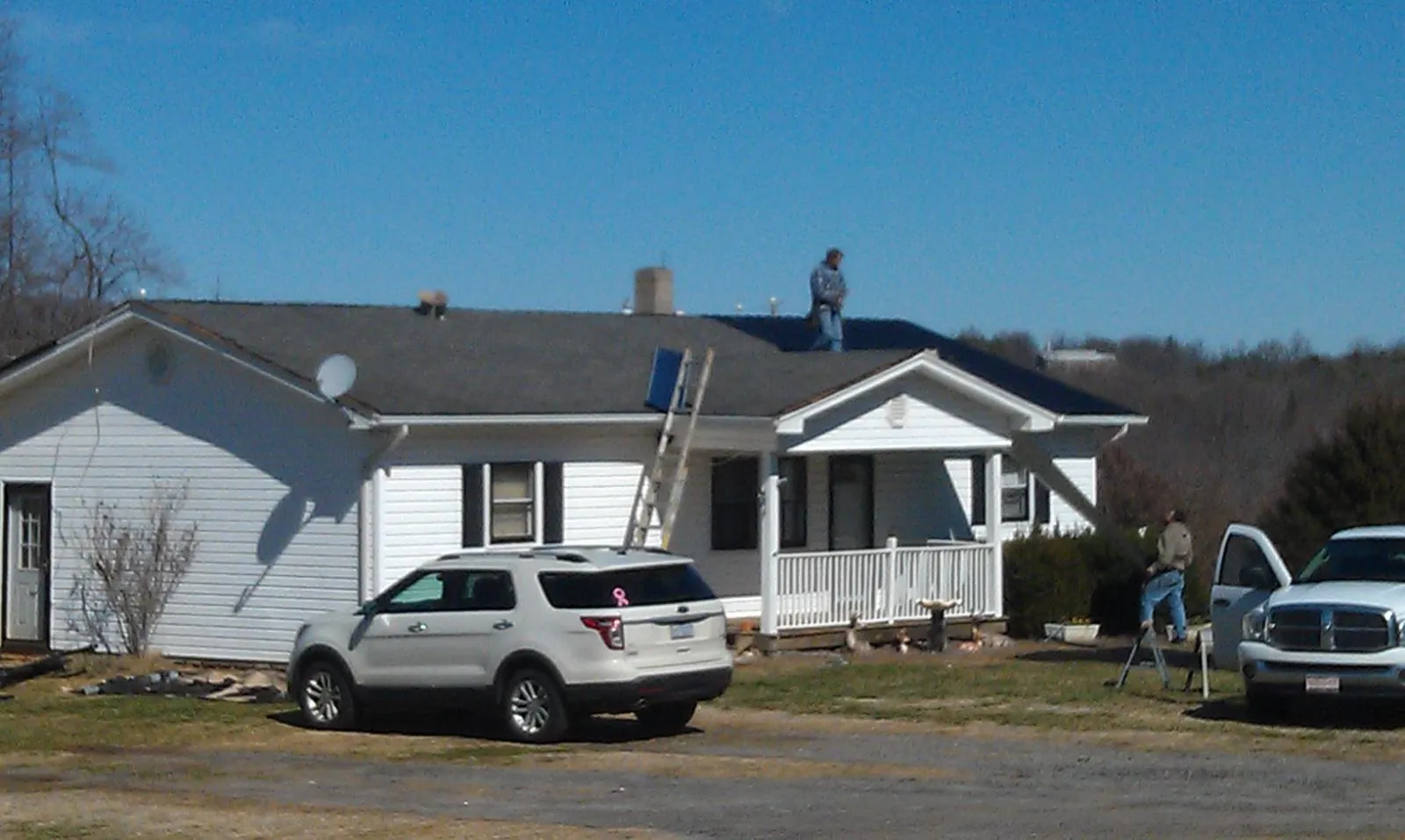 Roofers stripping shingles from a white ranch house roof in Beech Bluff