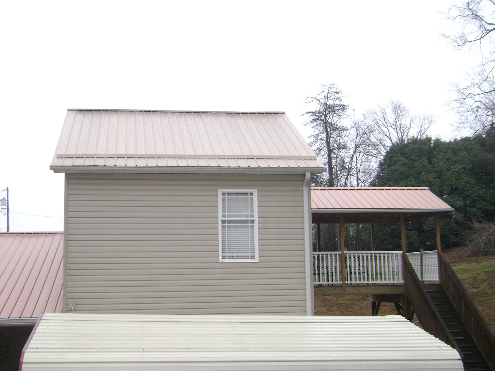 Tan metal roofs on a two story addition and attached porch, from a Roof Replacement job in Beech Bluff